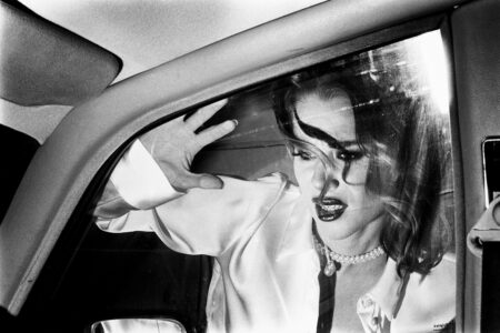 Woman peers through a car window with a shocked and angry expression, her hand pressed against the glass.